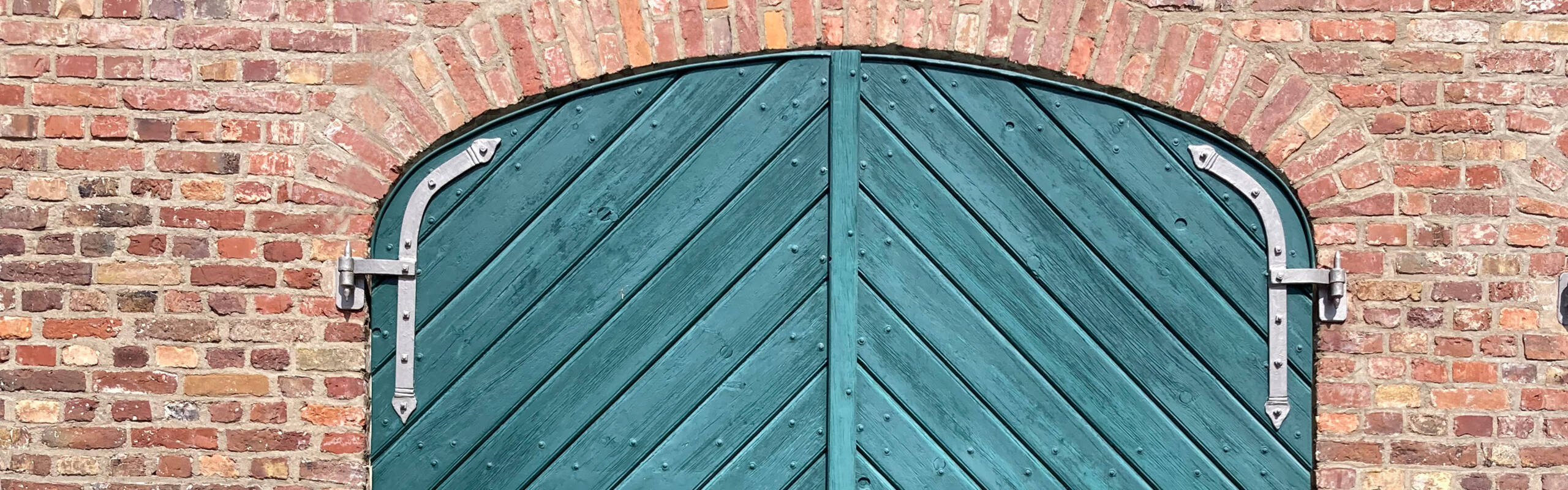 Der obere Ausschnitt einer alten blauen Holztür mit zwei Flügeln in einer Backsteinwand.